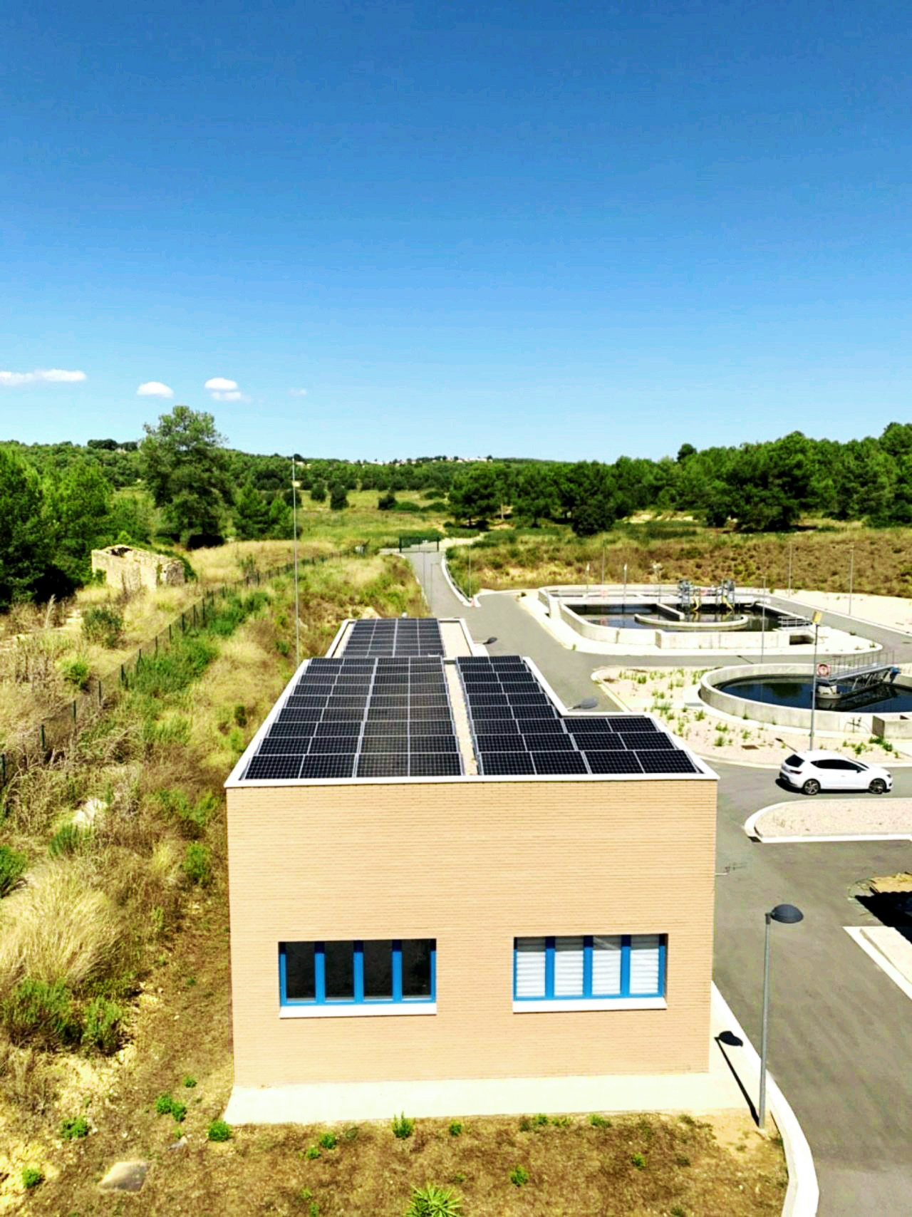 Ein Gebäude steht an einer einsmen Straße in einer sonnigen Landschaft. Vor dem Gebäude sind Klärbecken zu sehen.